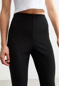 Hoge taille zwarte legging met een geribbeld textuur. De stof lijkt rekbaar en sluit strak aan om de taille en benen.