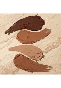 Four swatches of cream in varying shades from dark brown to light beige, displayed on a textured light marble surface.