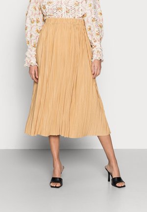 Vrouw draagt een beige geplooide midi-rok, een bloes met lange mouwen en bloemenprint met kanten details, en zwarte open teen hoge hakken mules.