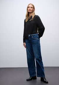 Sort skjorte med lange ærmer og leopardmønstrede sidedele, parret med bredbenede blå jeans og sorte ankelstøvler.
