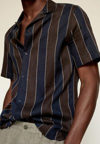 Camisa de manga corta con botones en rayas marrón oscuro y azul marino, confeccionada con tela texturizada, con cuello tipo campestre y sutiles detalles en gris.