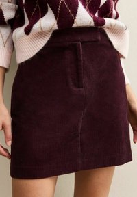 Bordeaux corduroy rok met een rechte snit, voorzien van een voorzak en textielstructuur, gecombineerd met een meerkleurige gebreide trui.