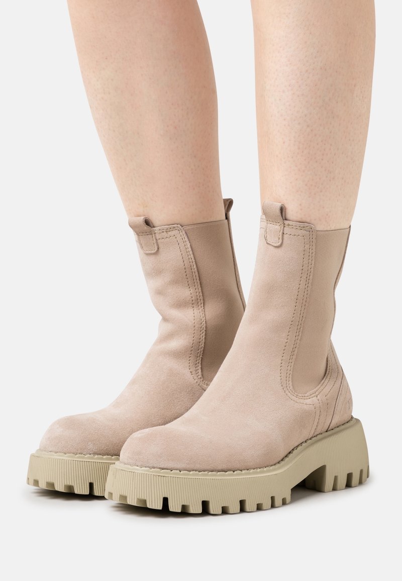 Bottines en daim beige avec panneaux latéraux élastiques et une semelle en caoutchouc beige épaisse et texturée. Finition douce avec des détails de couture minimaux.