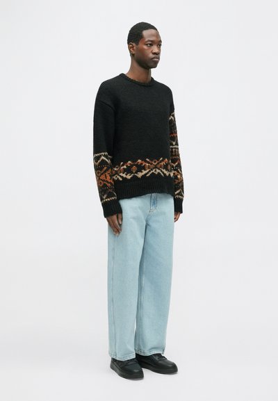 Fekete, kötött pulóver texturált anyagból, meleg színű mintázattal az alján, világoskék, bő szárú farmernadrággal párosítva.