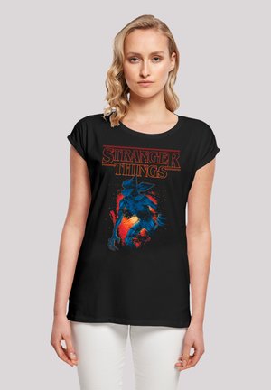 Schwarzes T-Shirt mit kurzen Ärmeln, das ein farbenfrohes "Stranger Things"-Grafikdesign zeigt, mit einer blauen Figur mit Krallen auf einem lebhaften Hintergrund.
