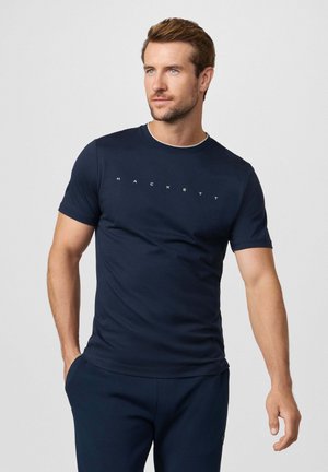 Camiseta de manga corta azul marino con cuello redondo y un sutil logo 'HACKETT' en color claro en el pecho. Textura de tela suave.