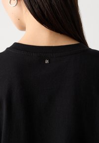 Μαύρο βαμβακερό μπλουζάκι με στρογγυλή λαιμόκοψη και μικρό λογότυπο DKNY ραμμένο στο πίσω μέρος, που παρουσιάζει �μια μαλακή, απαλή υφή.