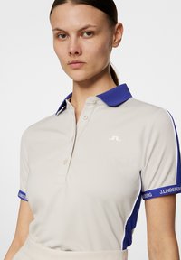 Beige polo skjorta med blå krage, i slim fit, kort ärm och märkta manschetter. Slät textur med knäppning.