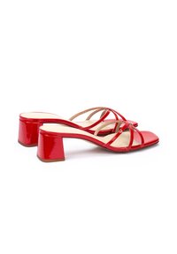 Talons aiguilles en cuir verni rouge avec un bout carré et de fines brides croisées. Le talon carré mesure environ 5 cm, offrant une stabilité.