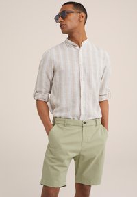 Svetlá, pruhovaná košeľa na gombíky s golierom, skombinovaná so svetlozelenými šortkami. Materiály sa zdajú byť priedušné a neformálne.