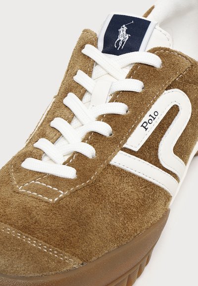 Baskets en daim marron avec des lacets blancs, une bande décorative blanche, et une étiquette logo Polo bleu marine sur la languette.