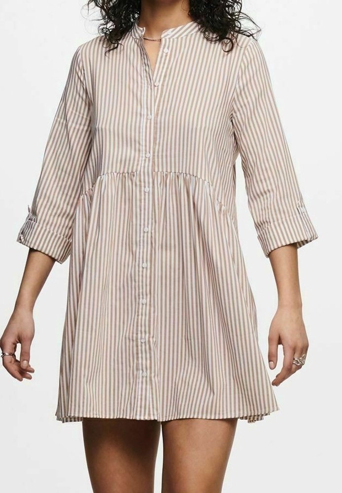 Femme portant une robe chemise rayée verticale beige et blanche, manches trois-quarts et taille froncée.
