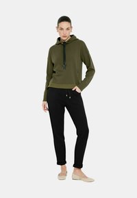 Felpa verde oliva con cappuccio e cordino, orlo a costine, e pantaloni neri. L'outfit ha una vestibilità comoda e include i polsini arrotolati sui pantaloni.