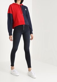 Sudadera recortada a rayas rojas y marino con cordón, combinada con jeans ajustados oscuros de tiro alto y zapatillas de plataforma blancas.