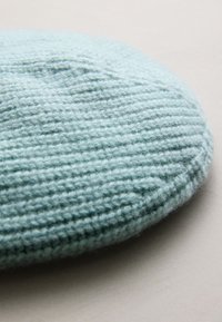 Knit beret in light blue, featuring a textured, ribbed pattern. Soft, wool-like material with a rounded, flat shape.