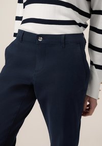 Marina-blå byxor tillverkade av lättviktsmaterial, med rak front, sidofickor och en silverknapp som stänger i midjan.