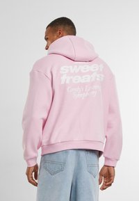 Pink hoodie featuring white text on the back reading "sweet treats" and "Candy's Loving Symphony." Material appears soft and cotton-like.