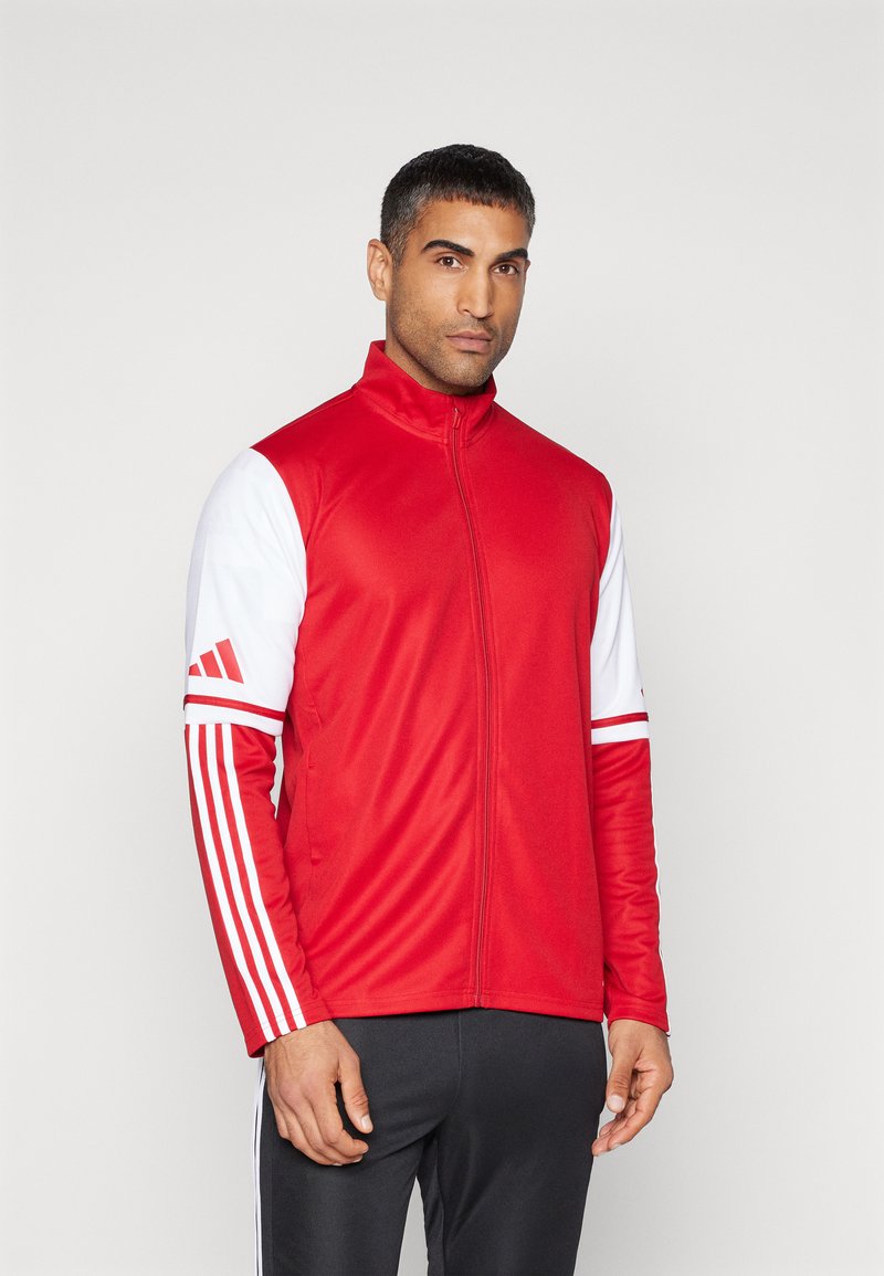 Rode sportjack met ritssluiting en witte mouwen, voorzien van drie strepen op elke arm en een hoge kraag. Glad textuur, atletische pasvorm.