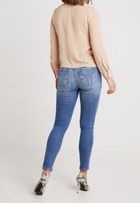 Beige long-sleeve top paired with blue skinny jeans and black-and-white patterned high-heeled shoes, viewed from the back.