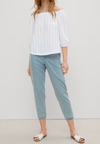 Top bianco, scollato sulle spalle, con texture e maniche corte a sbuffo abbinato a jeans azzurri svasati e sandali bianchi.