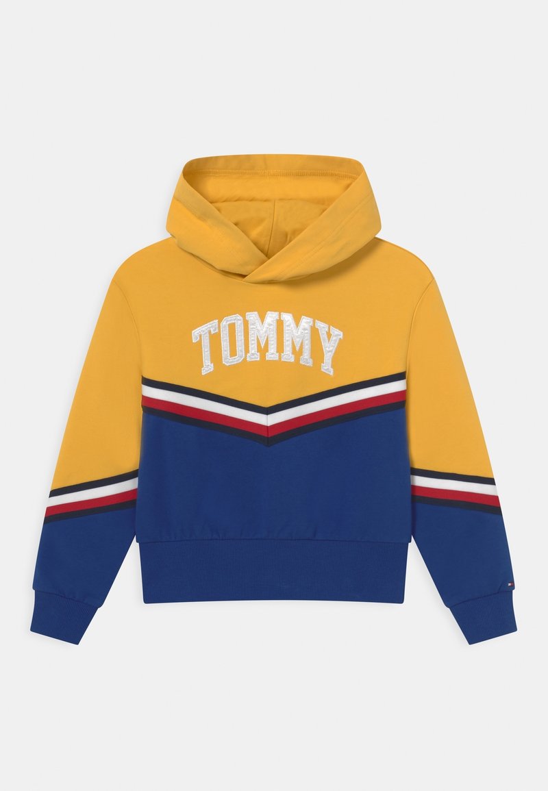 Sweat à capuche jaune et bleu avec une capuche, des bandes en chevron blanches, rouges et noires, et "TOMMY" brodé sur la poitrine.