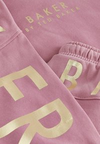 Różowa bluza z złotym napisem. Cechy to miękka tkanina, wygodne dopasowanie i elastyczne mankiety. Na metce widnieje napis "BAKER BY TED BAKER."
