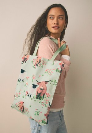 Torba na zakupy wielokrotnego użytku wykonana z trwałej tkaniny, z pastelowo zielonym tłem i zwierzęcym nadrukiem przedstawiającym krowy i owce wśród różowych kwiatów.