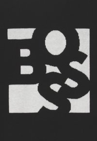 Černá textilie s velkým bílým grafickým designem. Design obsahuje geometrické tvary a stylizovaná písmena integrována do vzoru.
