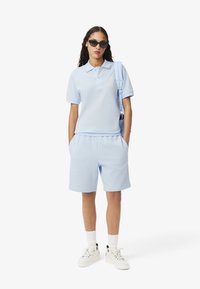 Polo azzurro chiaro e pantaloni coordinati, realizzati in tessuto morbido. Presenta un colletto classico, tasche e abbinato a sneakers bianche.