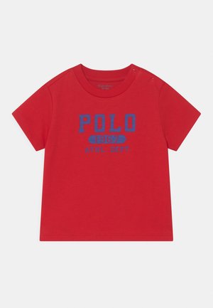 Červené bavlněné tričko s krátkými rukávy, na přední straně modrý potisk "POLO 1967 ATHL. DEPT." a dvě druky na levém rameni.