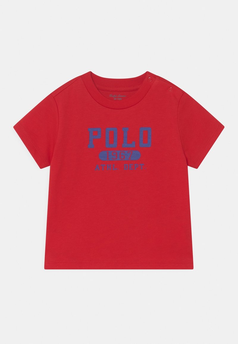 Červené bavlněné tričko s krátkým rukávem, s modrým textem "POLO 1967 ATHL. DEPT." Límec má patentky pro snadné oblečení.