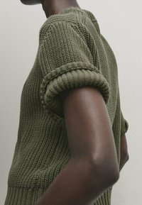 Strikket top i olivengrøn med korte, op rullede ærmer. Mønstret struktur over det hele og ribbet detalje ved halsudskæring og kant.