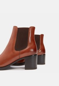 Pruunid nahast ankle-kotid sujuva viimistlusega, elastsete külgpaneelidega ja massiivse musta kannaga, mis näitab nutikat ja modernset disaini.