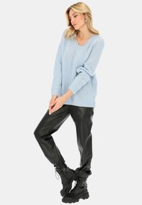 Jasnoniebieski sweter z dzianiny z dekoltem w serek, z długimi rękawami i ściągaczami na mankietach, w połączeniu z czarnymi spodniami z ekoskóry i masywnymi czarnymi botkami.