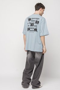 Blue cotton oversized T-shirt featuring a large black text print on the back. Paired with loose-fitting gray denim pants.