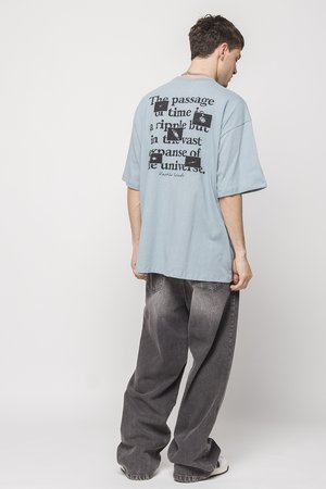 Blue cotton oversized T-shirt featuring a large black text print on the back. Paired with loose-fitting gray denim pants.