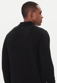 Cappotto nero lavorato a maglia con colletto, maniche lunghe e design aderente. Presenta una texture liscia e una silhouette posteriore sagomata.