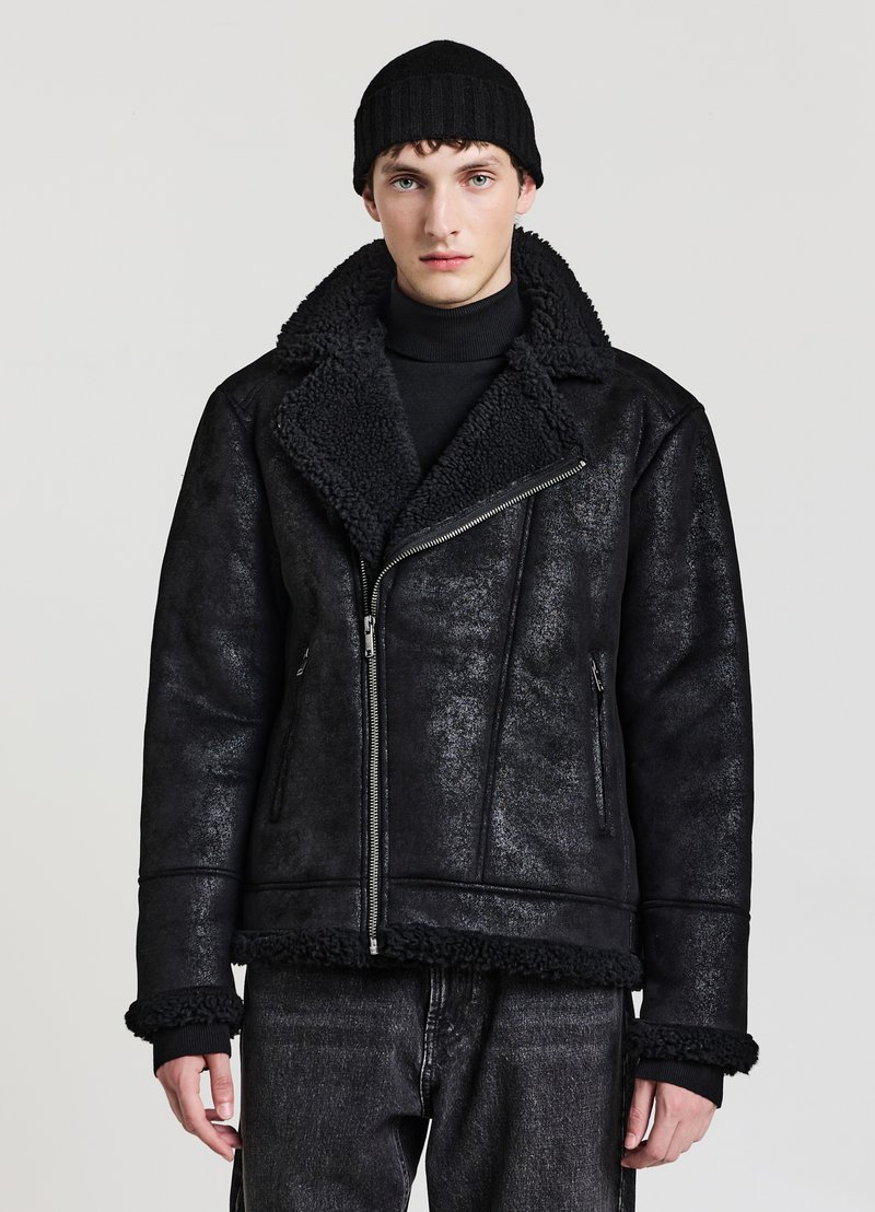 Giacca nera in ecopelliccia con chiusura a zip, ampio colletto e finitura testurizzata. Presenta polsini aderenti e rifinitura in pile a contrasto.