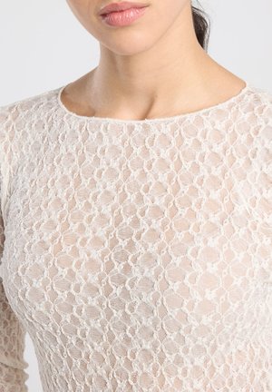 Kanten top in lichtcrème met een gestructureerd honingraatpatroon. Lange mouwen en een ronde halslijn. Doorszichtig materiaal met een delicate afwerking.