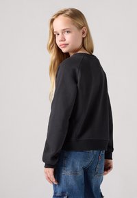 Felpa nera con maniche lunghe, polsini e orlo a costine. Il retro presenta un collo arrotondato, abbinato a pantaloni in denim blu sbiadito.