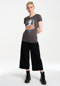 Gray t-shirt featuring a colorful Wonder Woman graphic, paired with black wide-leg pants and black lace-up boots. Smooth fabric texture.