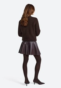 Brown ribbed sweater paired with a flared, glossy dark purple skirt. Black tights and patent heels complete the look. Back view displayed.