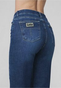 Mørkeblå denimjeans med en slank passform. Funksjoner inkluderer en baklomme med en grå logolapp og subtile stingdetaljer.