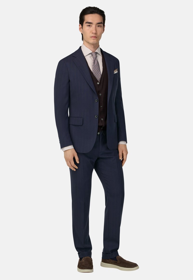 Tumes sinine triibuline ülikond, millel on lõigatud kraed, pruun vest ja valge triibuline särk. Viimistletud mustrilise lipsu ja pruunide kingadega.