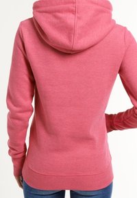 Sudadera con capucha de forro polar en rosa claro con un bolsillo delantero tipo canguro, capucha con cordón, puños acanalados y dobladillo con banda, vista desde atrás.