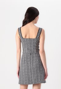 Robe à carreaux noir et blanc avec un décolleté carré, des bretelles larges, un corsage ajusté et une jupe évasée, fabriquée en tissu texturé.