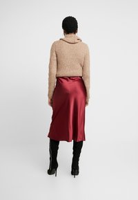 Suéter de punto beige con cuello de cisne, combinado con una falda midi de satén burdeos. Complementado con botas altas de tacón negro.
