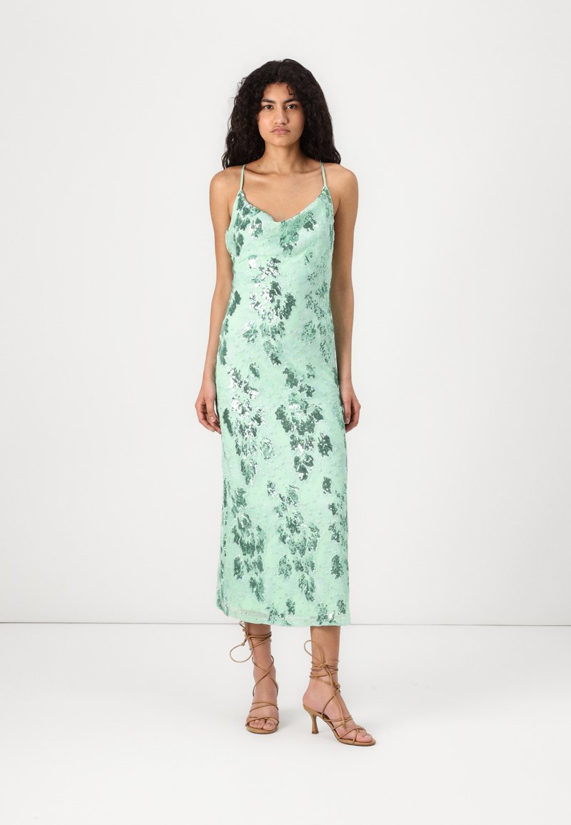 Mintgrünes, ärmelloses Satin-Maxikleid mit Blumenmuster und gewelltem Ausschnitt. Das Model trägt dazu leichte, braune Riemchenschuhe.