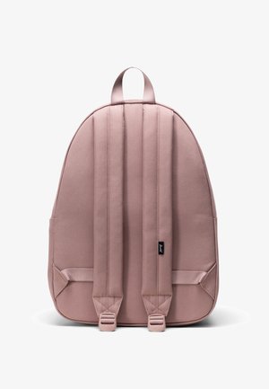 Vaalea vaaleanpunainen reppu, joka on valmistettu kankaasta ja jossa on pehmustetut hihnat, ylälenkki, sivutaskut ja tyylikäs, pyöristetty muoto. Varustettu pienellä mustalla logotagilla.