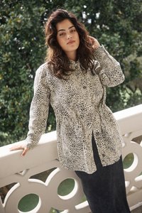 Leopard print button-up shirt with a cinched waist, long sleeves, and a collar, paired with a dark, long skirt against a balcony railing.
